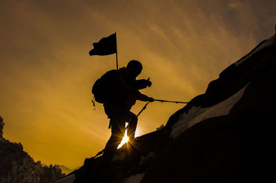 Low angle view of silhouette man hiking on mountain against sky during sunset