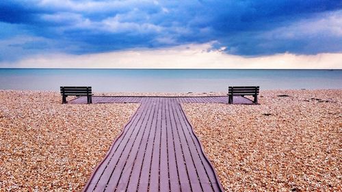 Deck chairs on beach against sky