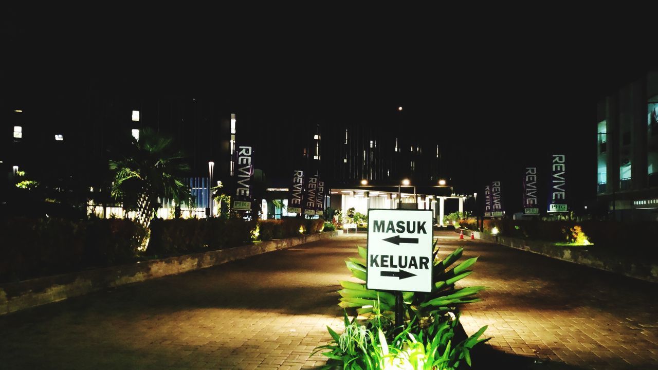 INFORMATION SIGN ON STREET BY ILLUMINATED BUILDINGS AGAINST SKY