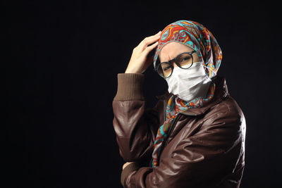 Portrait of woman in hijab with headache standing against black background