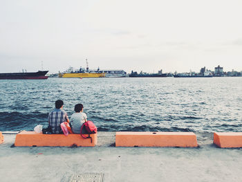 Rear view of men sitting on sea against sky