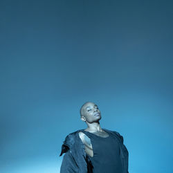 Bald young woman with eyes closed standing against blue background