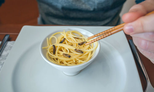 Midsection of man having noodles and worms in restaurant