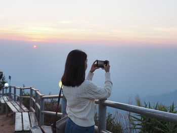 Rear view of person photographing against sky during sunset