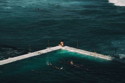 People in swimming pool against calm blue sea