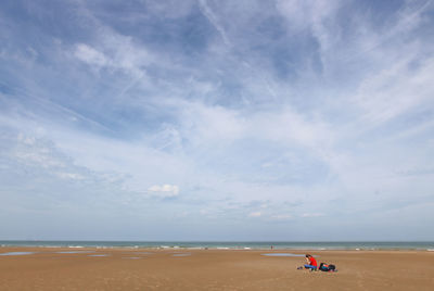 Scenic view of a woman sitting on a beach against sky