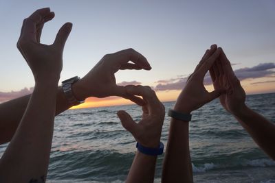 Close-up of hands against sea at sunset