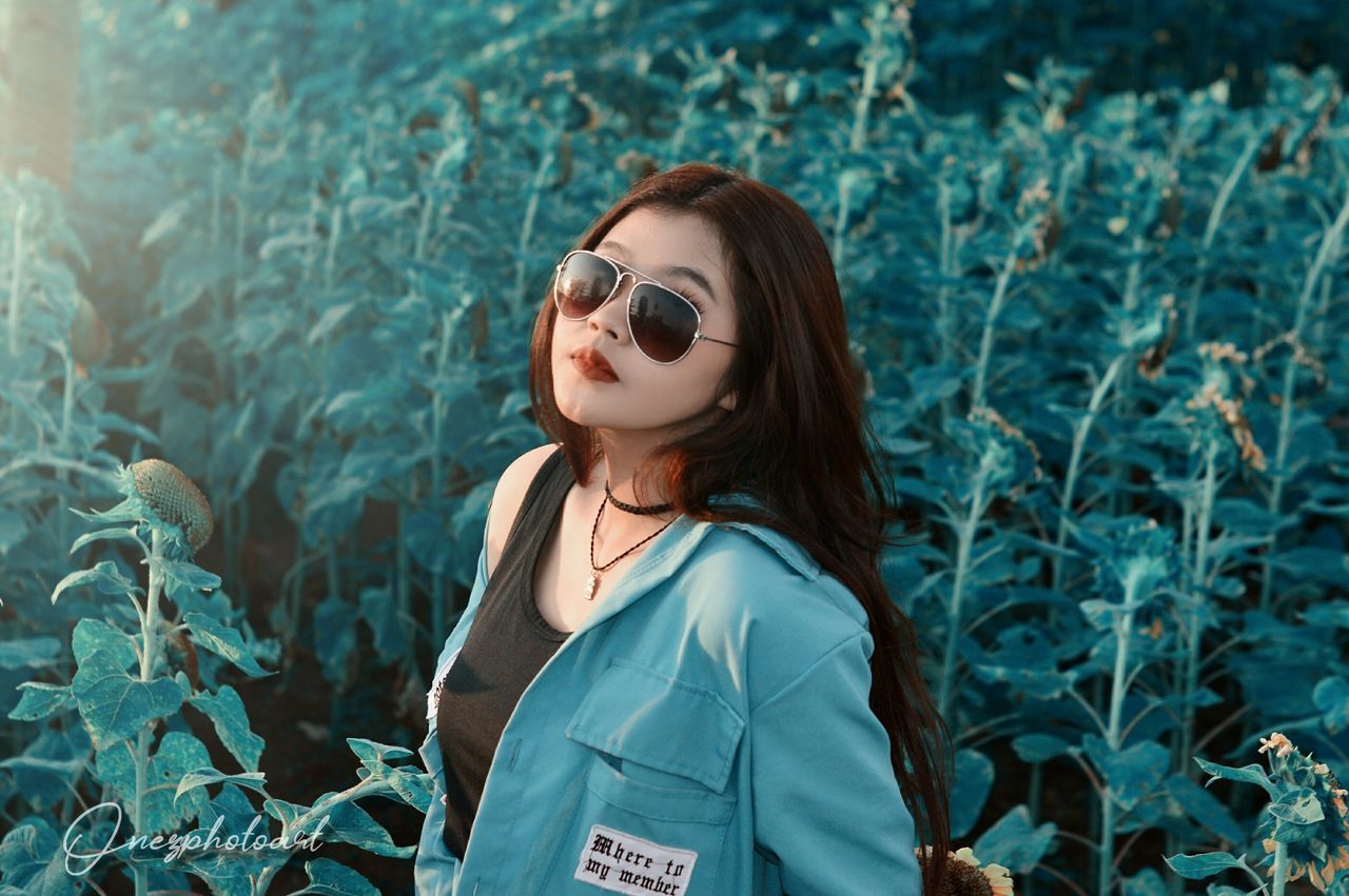 PORTRAIT OF WOMAN STANDING BY PLANTS