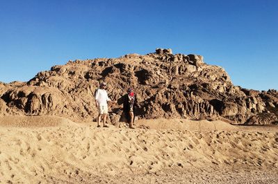 Rear view of people standing on rock formation against clear sky