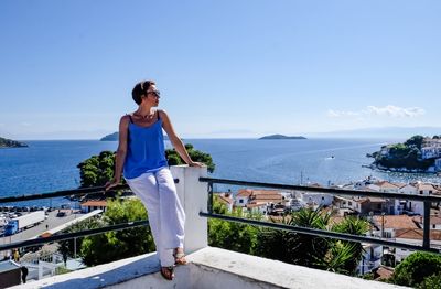 Woman sitting on railing against sea