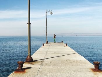 Mid adult woman standing on pier by sea against sky