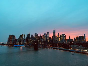 Brooklyn bridge over east river by illuminated buildings in city against sky