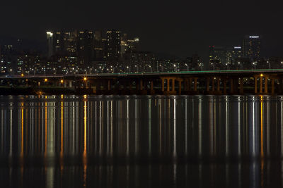 Lights reflecting by bridge over river in city at night
