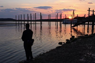 Rear view of silhouette man standing by river against sky