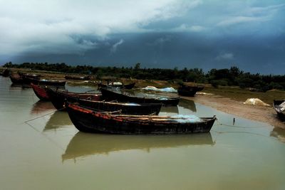 Boats in river against cloudy sky