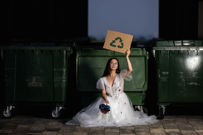 Beautiful young bride in her wedding dress holding a sign that says save the world and recycling