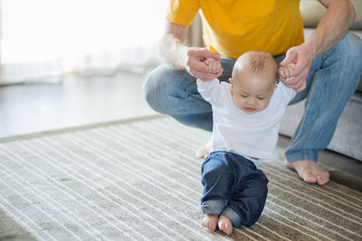 Low section of father holding cute son standing on carpet