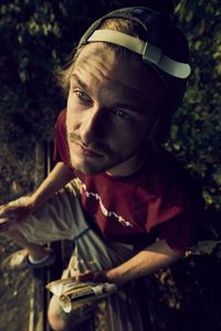 High angle view of young man looking up while sitting on log in forest