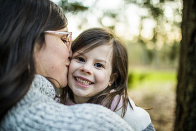 Close up view of mother kissing and hugging young cute daughter.