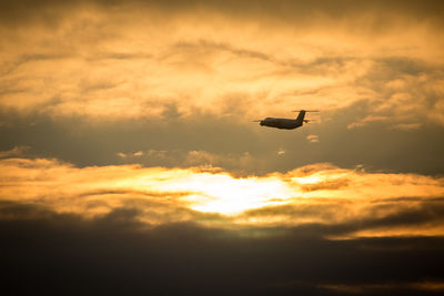 Low angle view of silhouette airplane flying against sky during sunset