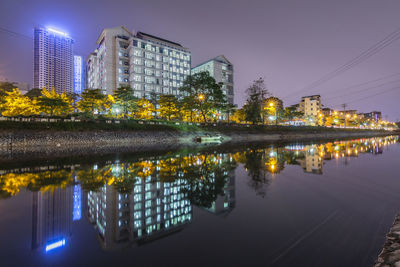 Illuminated buildings by lake against sky in city at night