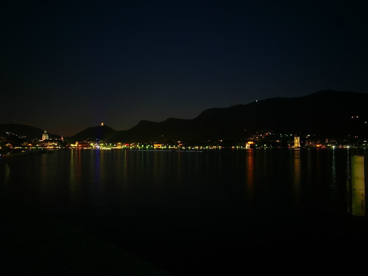 LAKE BY ILLUMINATED MOUNTAIN AGAINST SKY AT NIGHT