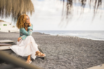 Smiling woman looking at sea while sitting on lounge chair