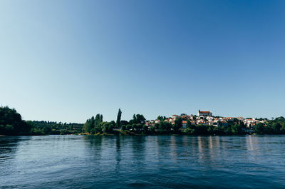 Scenic view of river by buildings against clear blue sky