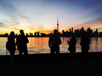 Silhouette people standing by sea against sky during sunset