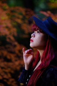 Side view of thoughtful redhead woman with hat against trees