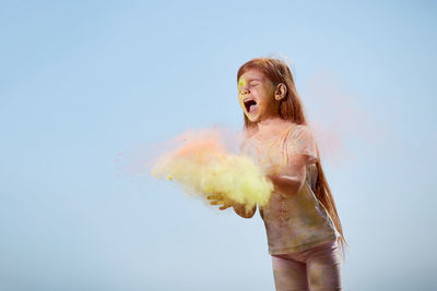 Smiling girl playing with powder paint against sky
