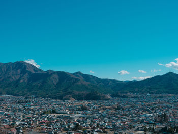 Aerial view of townscape by mountains against blue sky