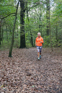 Senior woman jogging on autumn leaves at field in forest