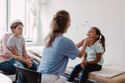 Female doctor examining smiling girl while family sitting in medical room