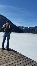 Man standing on pier over frozen lake against mountains