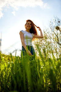 Young woman standing amidst plants on field against sky