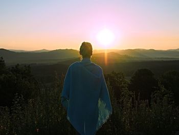 Rear view of woman standing on mountain during sunset