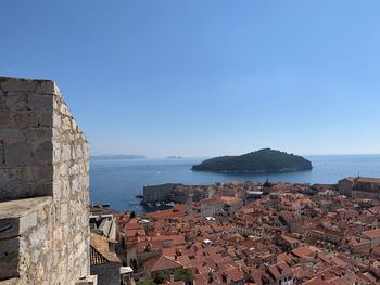 Buildings by sea against clear blue sky