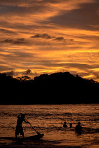 Silhouette man paddleboarding on sea against sky during sunset