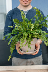 A male gardener holds an indoor fern in a clay pot in his hands. transplanting houseplants.