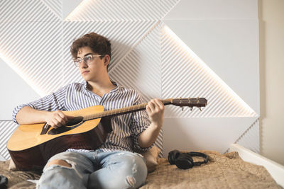 Young man playing guitar while sitting on sofa at home