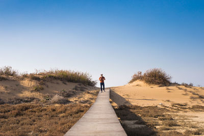 Rear view of man walking on street against clear sky