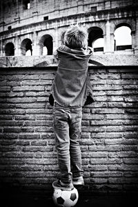 Rear view of boy standing on soccer ball while looking at coliseum