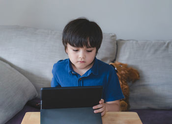 Cute boy using digital tablet while sitting on sofa at home