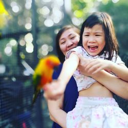Cheerful girl with mother holding parrot