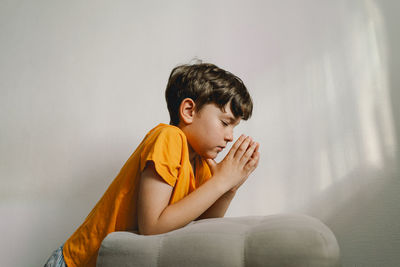 A boy in an orange t-shirt prays at home. concept for faith