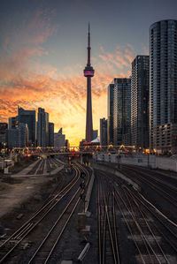 View of railroad tracks and buildings in city during sunset