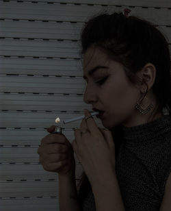 Close-up of young woman lighting cigarette against wall