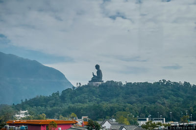 Statue by trees and buildings against sky