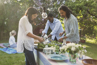 Friends preparing food at dining table in backyard during summer party